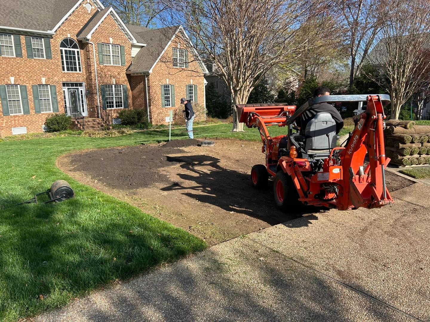 Red tractor working on a gravel driveway beside a brick house and lawn