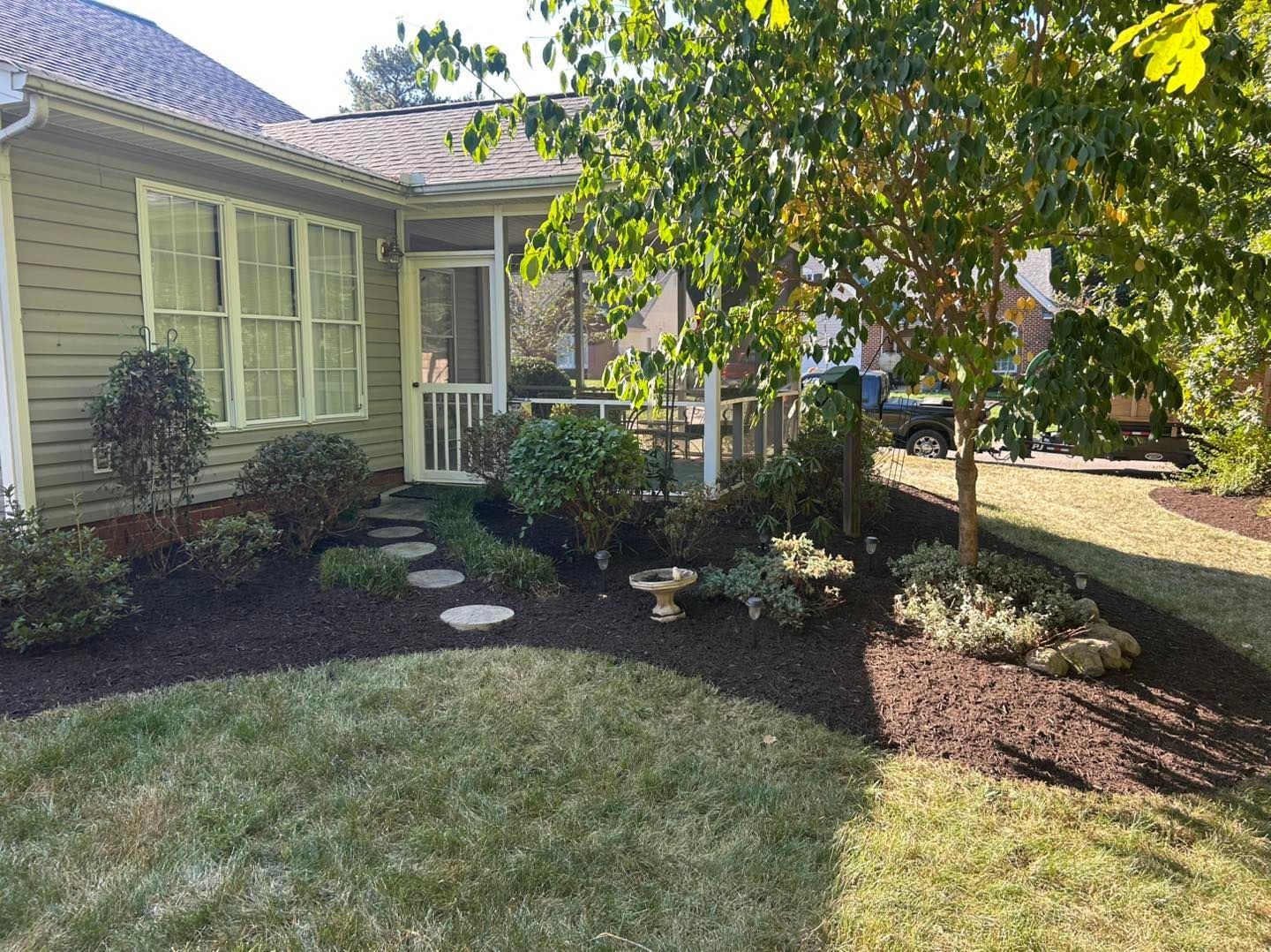 Front yard garden with a house, trees, shrubs, and stepping stones in sunlight