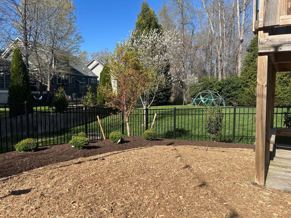 A brick house stands behind a freshly cleared, bare dirt patch in a residential front yard with a tractor on the right.