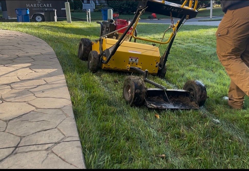 Yellow lawn machine on grass near a stone walkway, with a worker standing beside it outdoors.