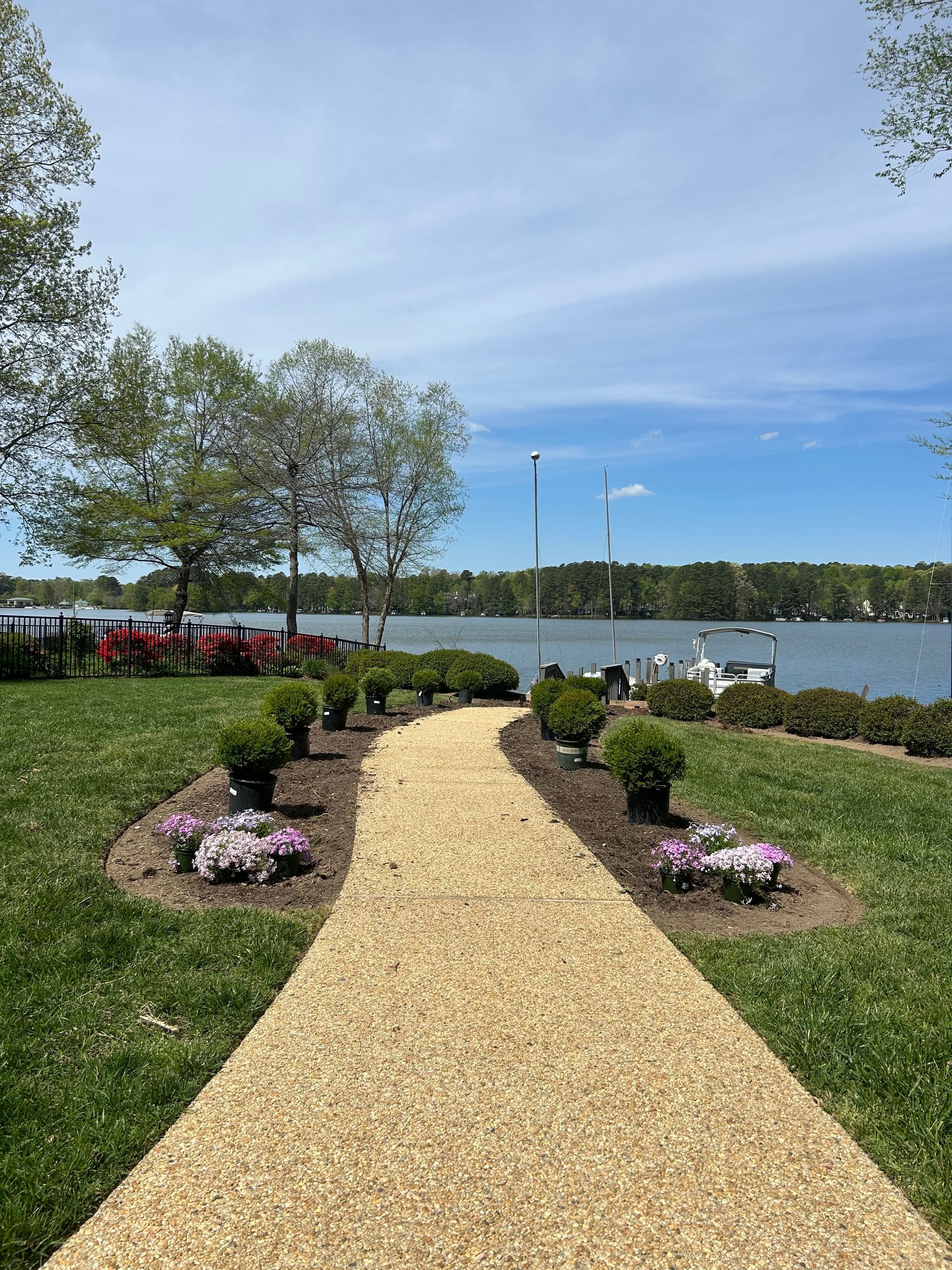 Gravel garden path lined with flowers leading to a lake on a sunny day