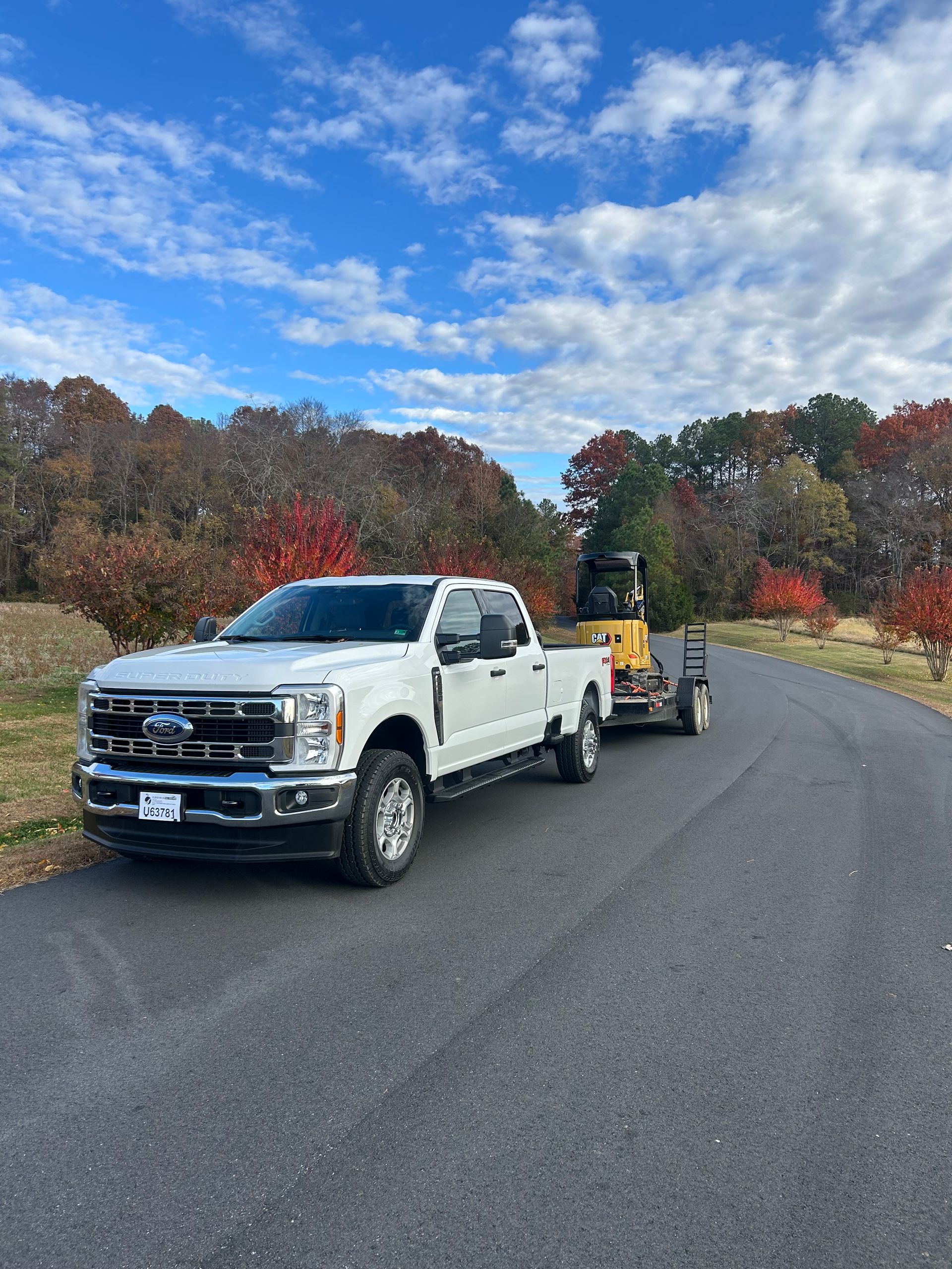 White pickup towing a small trailer on a curved road under a cloudy autumn sky