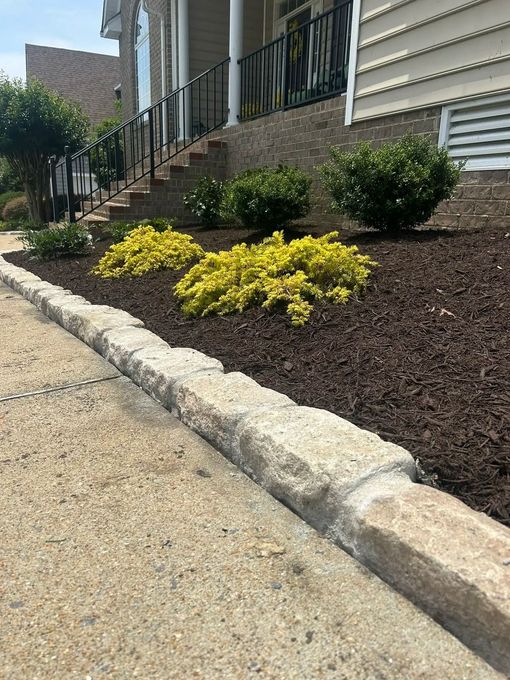 A suburban home with white siding and a driveway next to a landscaped garden bed containing shrubs and a mailbox.