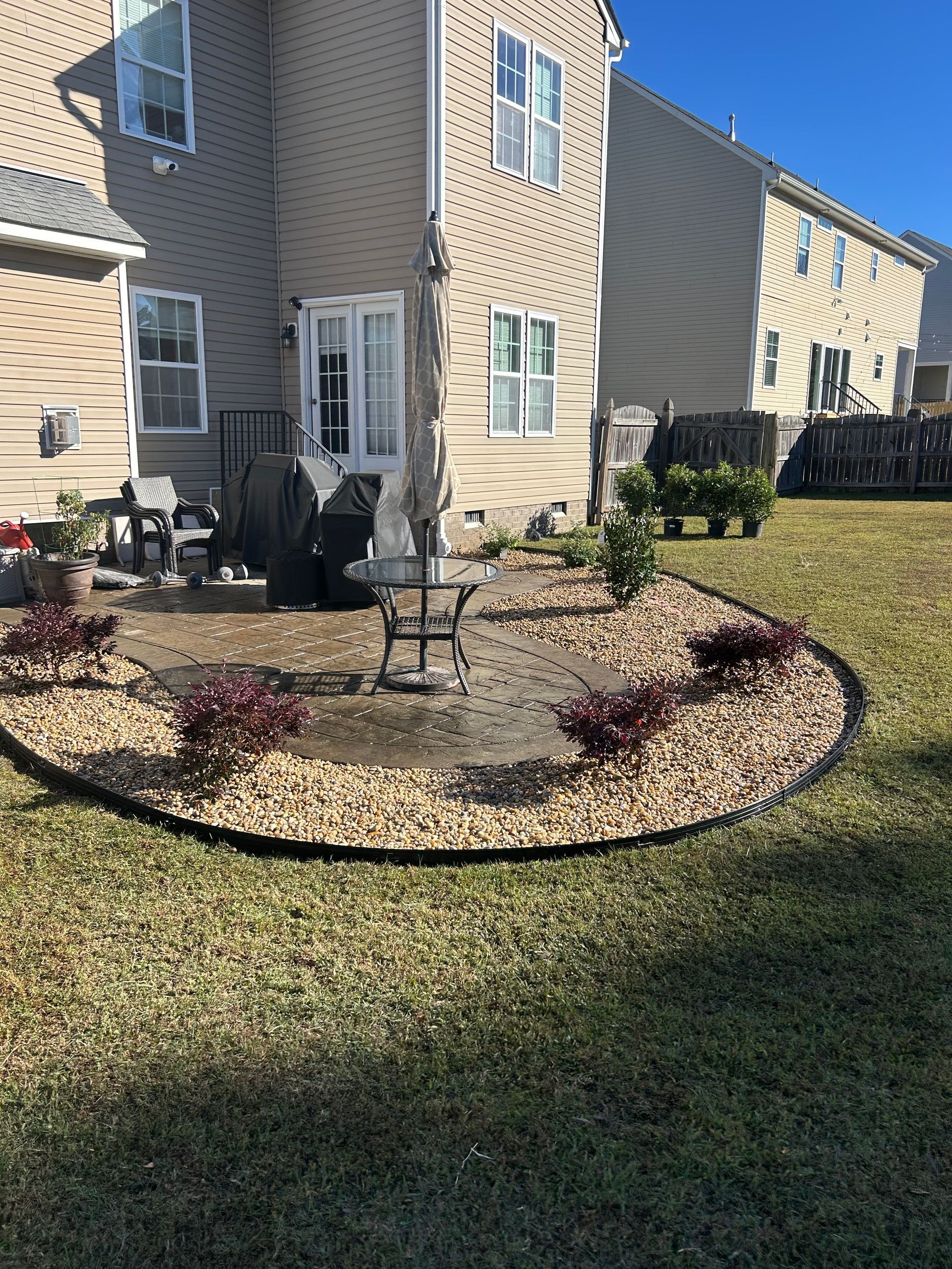 Front yard landscaping with a small tree, gravel border, and beige townhouses in bright sunlight