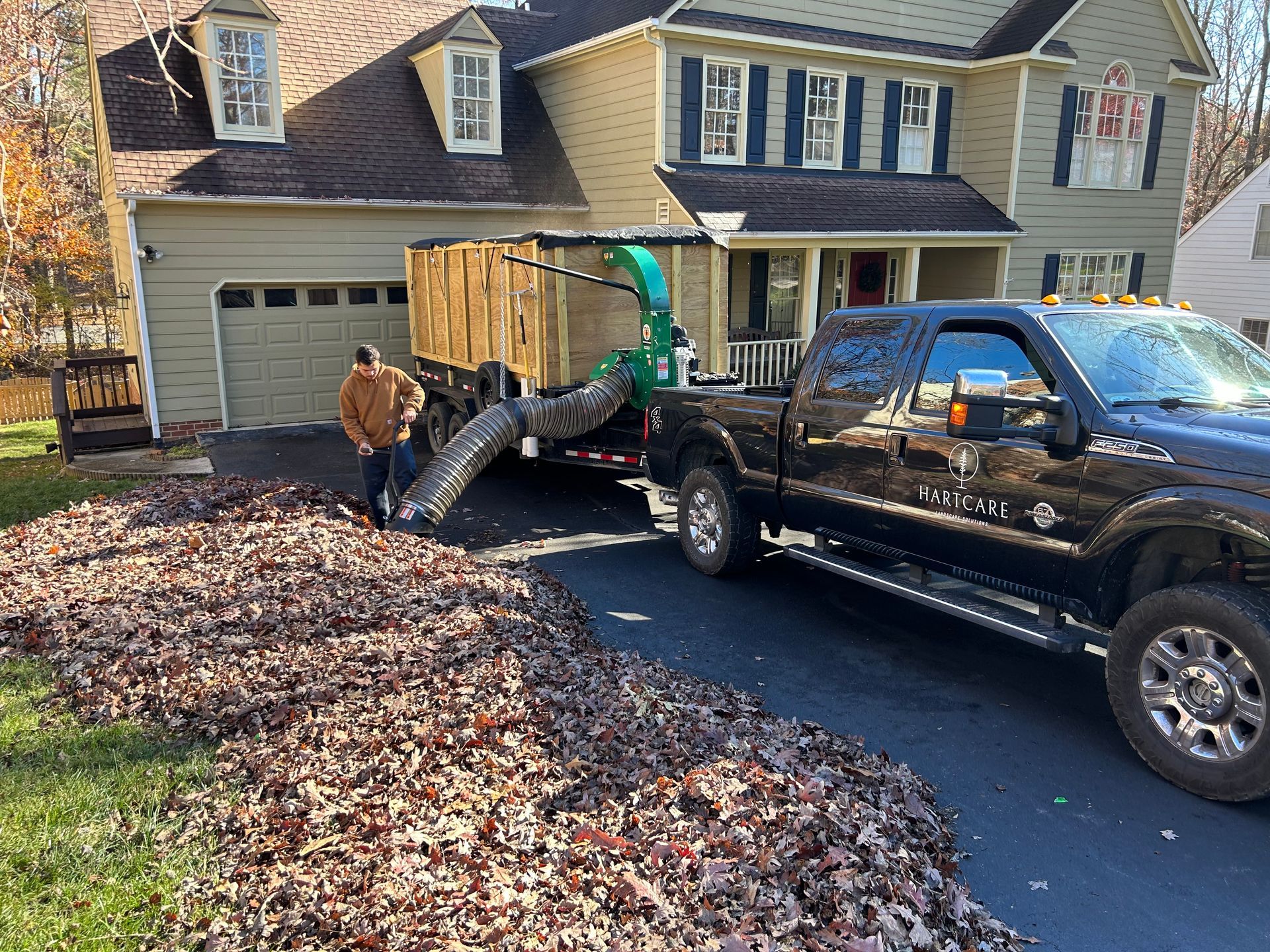 Worker loading a large crate from a dump trailer into a black pickup in a suburban driveway
