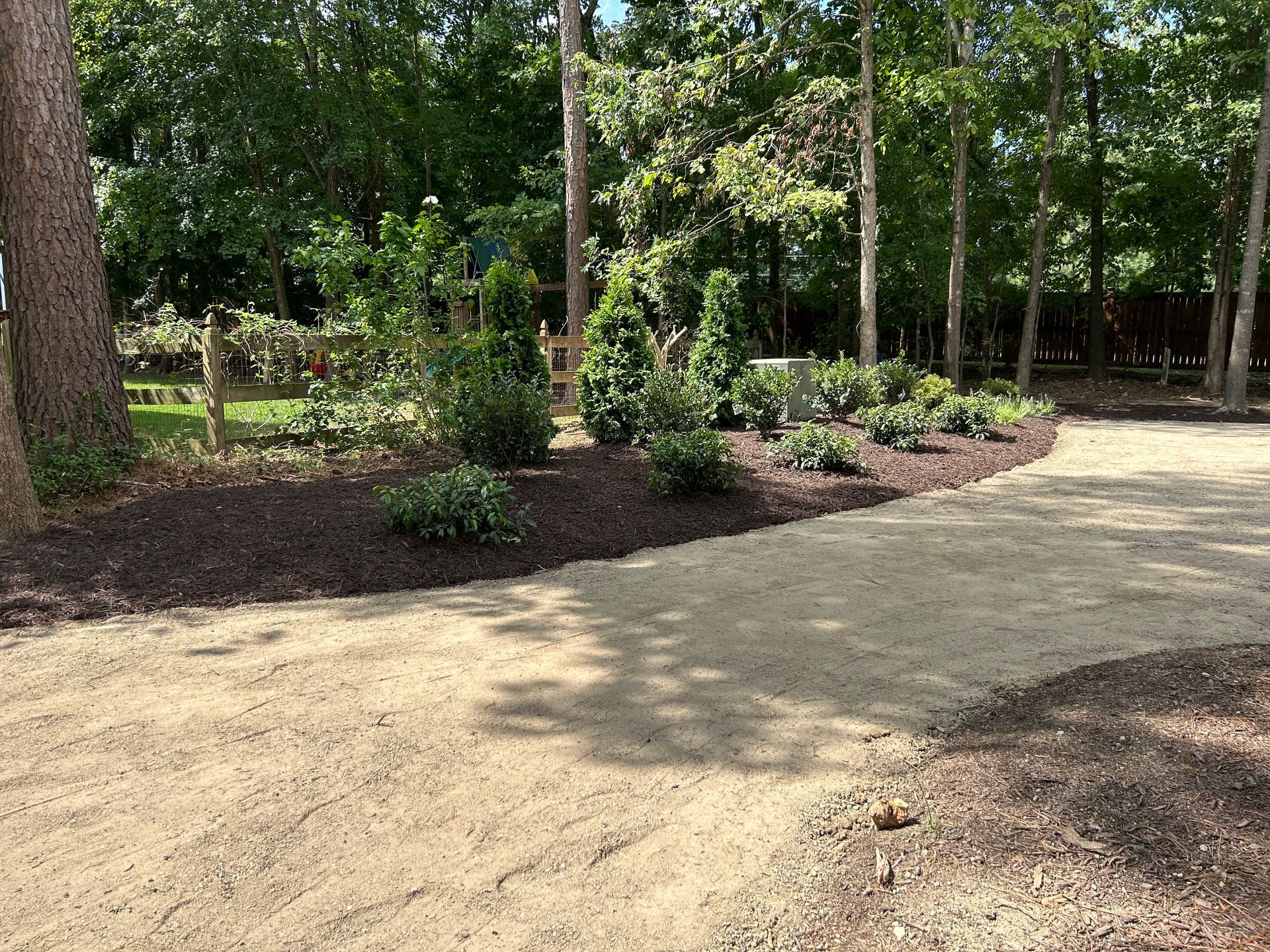 Curved dirt path through a wooded park with trees, shrubs, and dappled sunlight