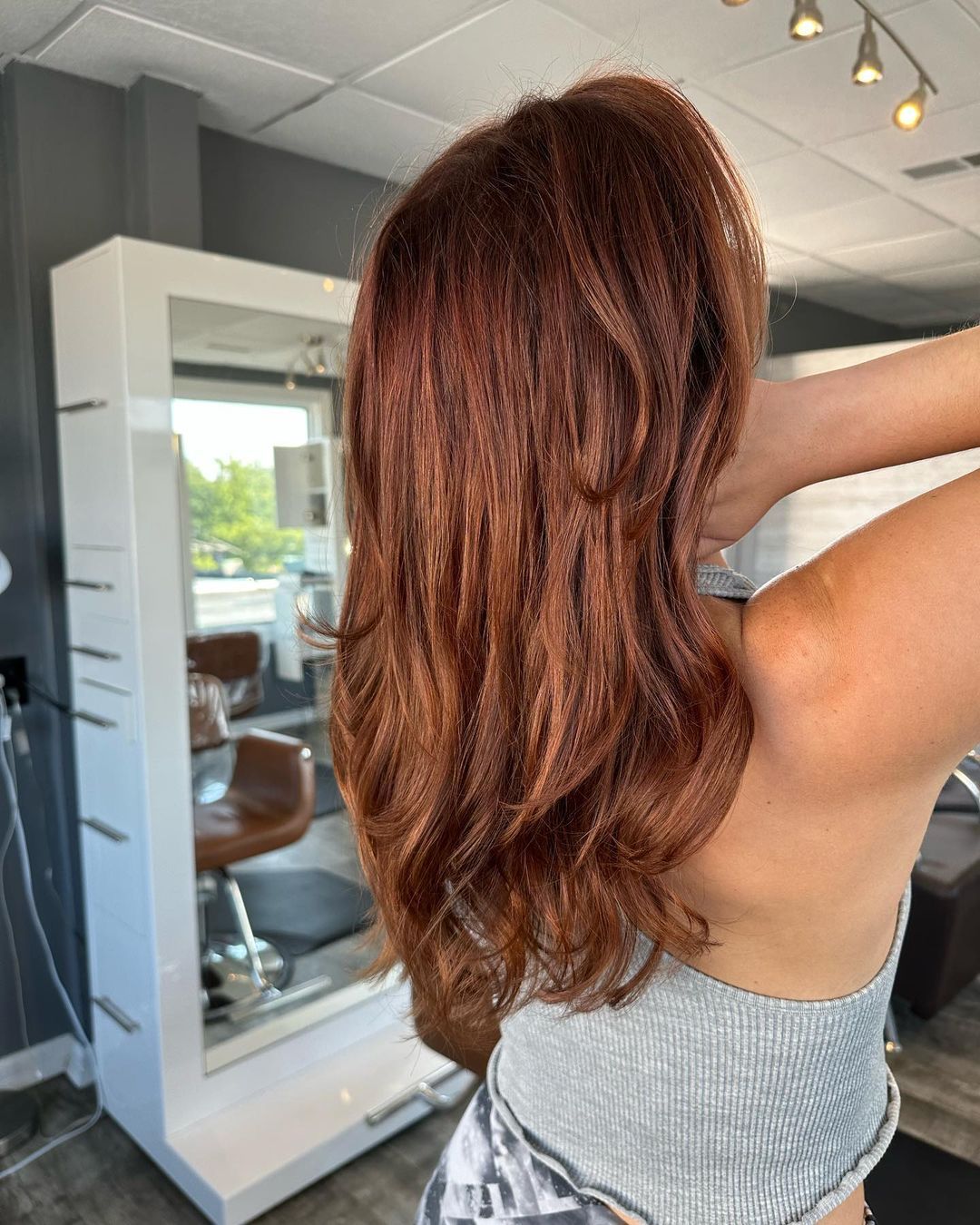 A woman with red hair is standing in front of a mirror in a salon.