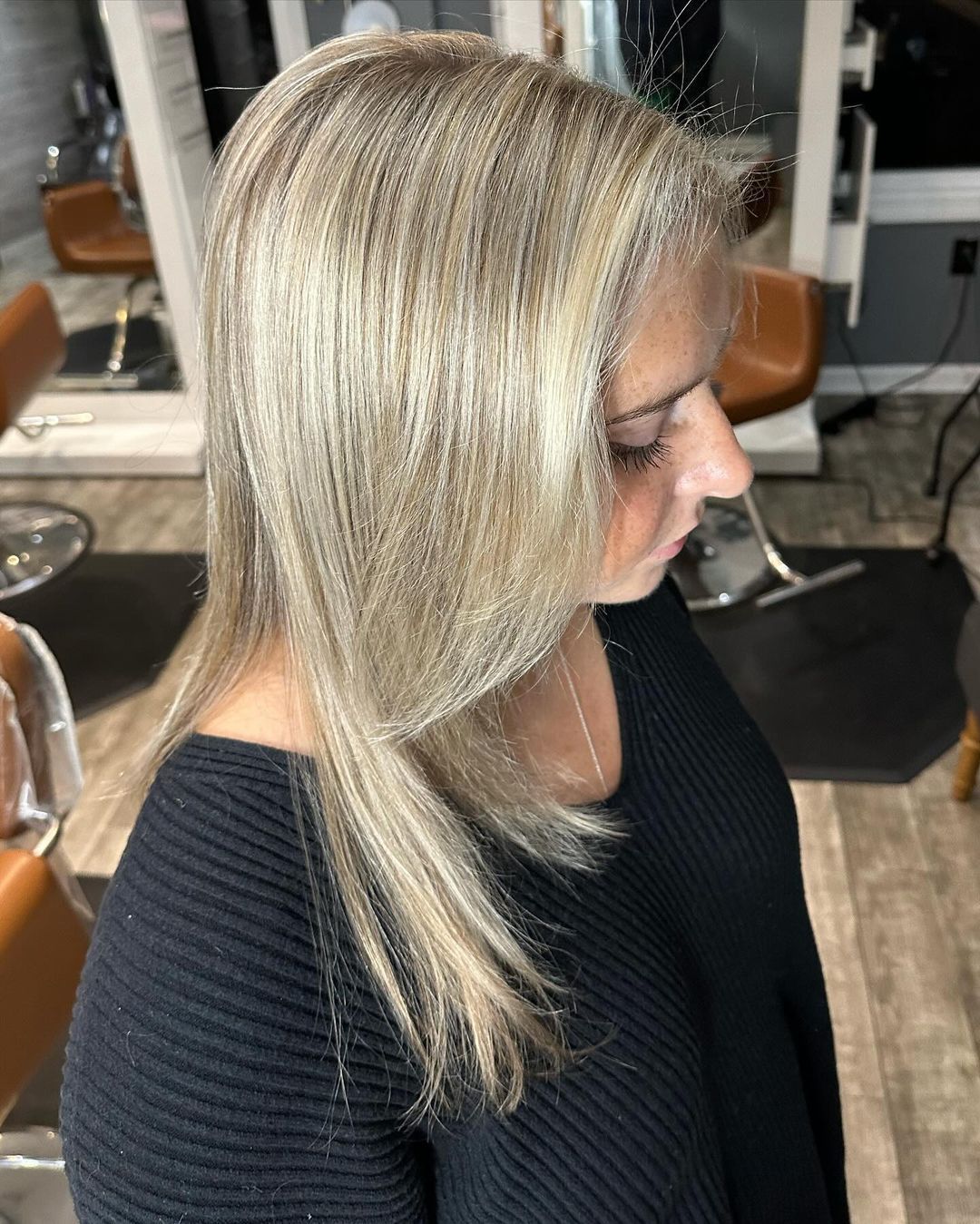 A woman with long blonde hair is sitting in a chair in a salon.