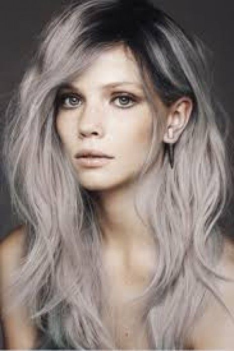 A woman with long gray hair is wearing a wig and earrings.