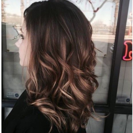 A woman with long brown hair is standing in front of a window.