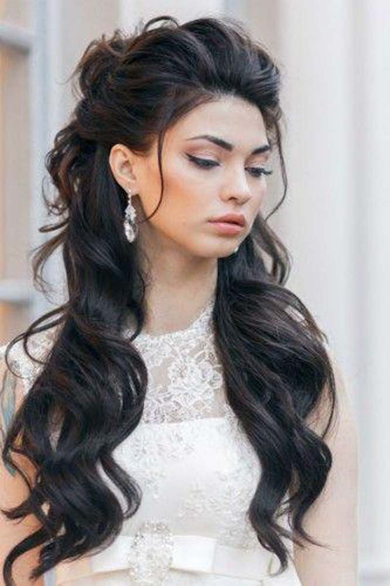 a woman with long dark hair is wearing a white dress and earrings .