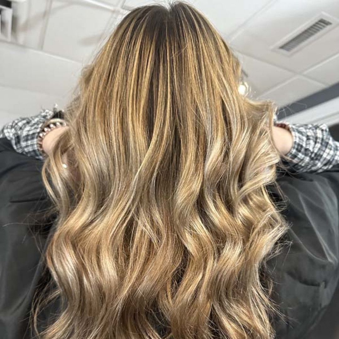 A woman with long blonde hair is sitting in a chair with her hands behind her head.