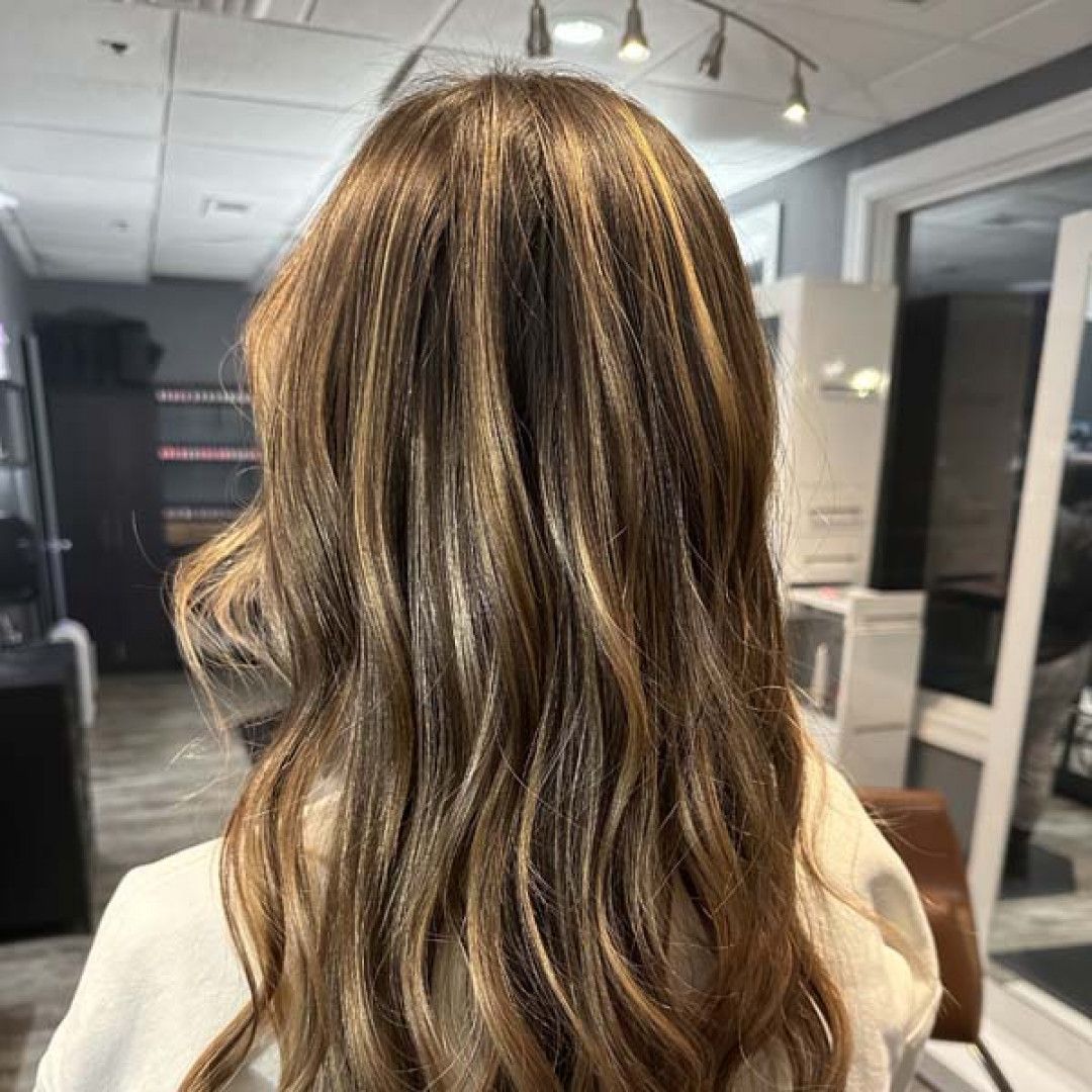 A woman with long brown hair is sitting in a chair in a salon.