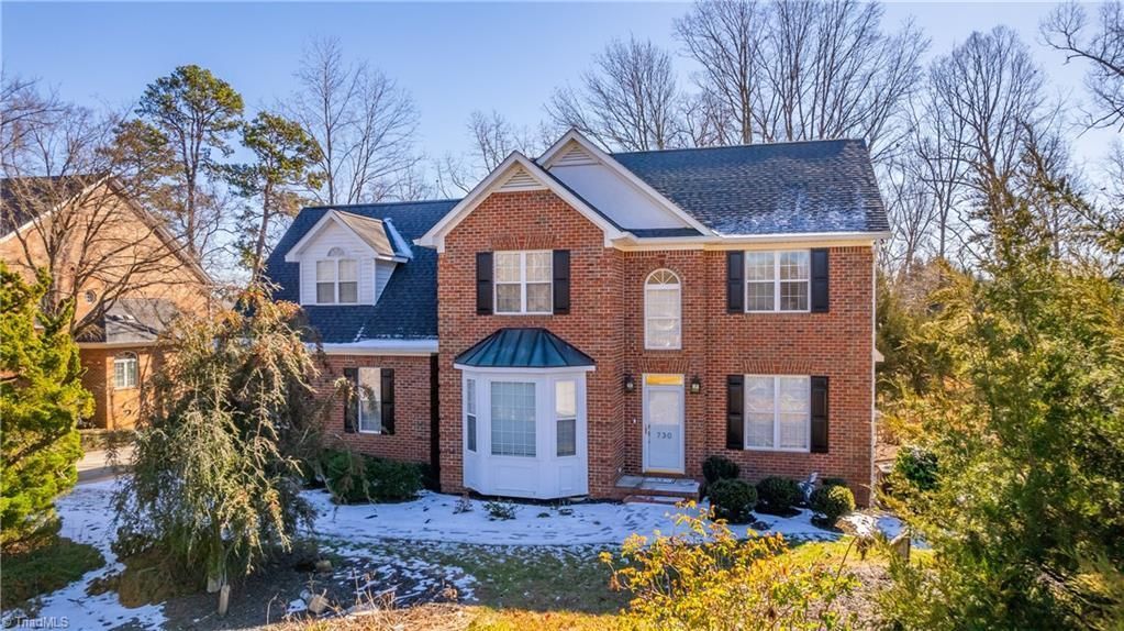 Two-story brick house with white trim and snowy front yard among leafless trees