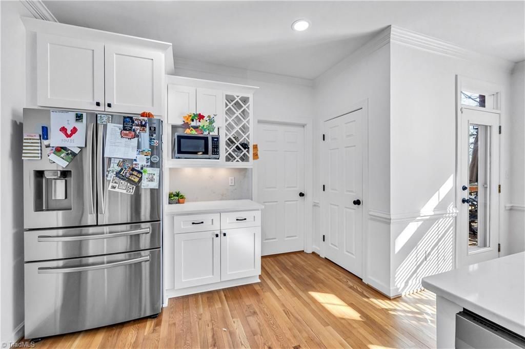 Bright white kitchen with stainless steel fridge, wood floors, and sunlight through a window.
