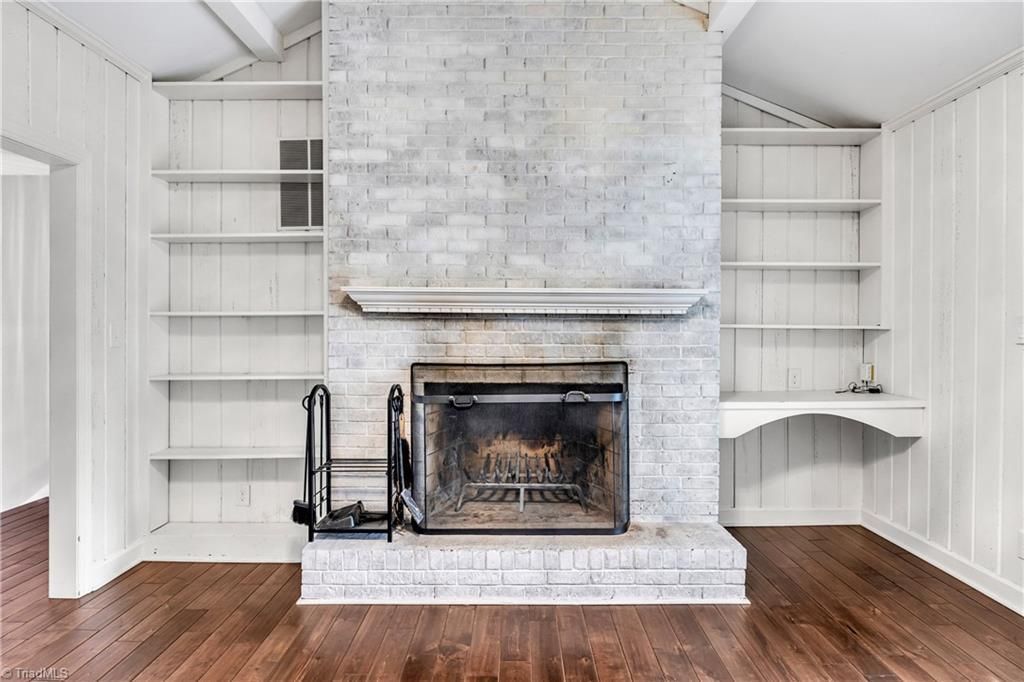Bright living room with white built-in shelves flanking a large white brick fireplace and hardwood floor.