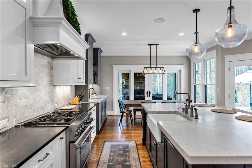 Bright modern kitchen with white cabinets, marble island, pendant lights, and a dining area beyond.