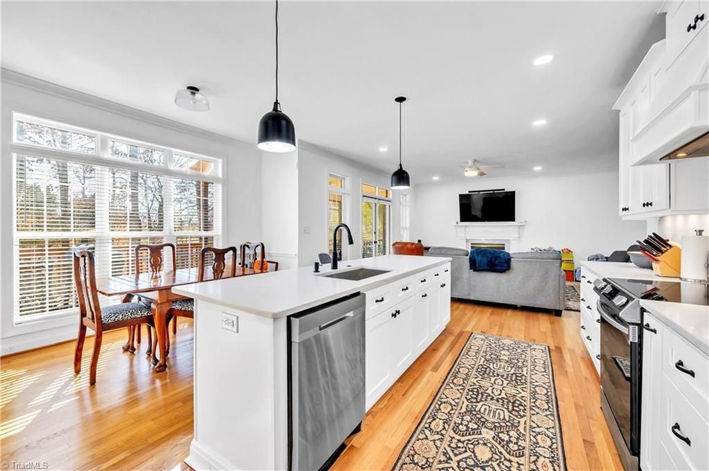 Bright modern kitchen and dining area with white cabinets, island, wood floors, and a gray sofa in back