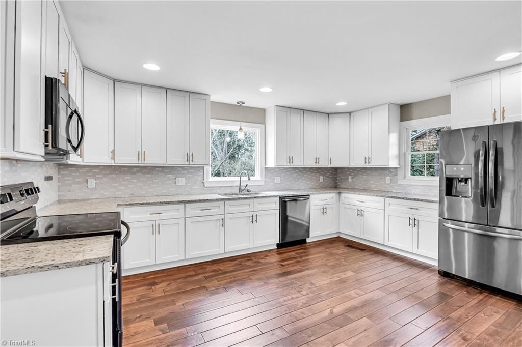 Bright, modern white kitchen with stainless steel appliances, granite counters, and hardwood floors