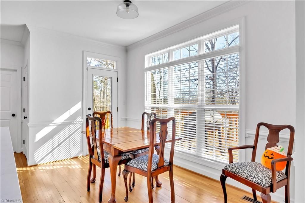 Bright sunlit dining room with wooden table, chairs, and large windows overlooking a deck