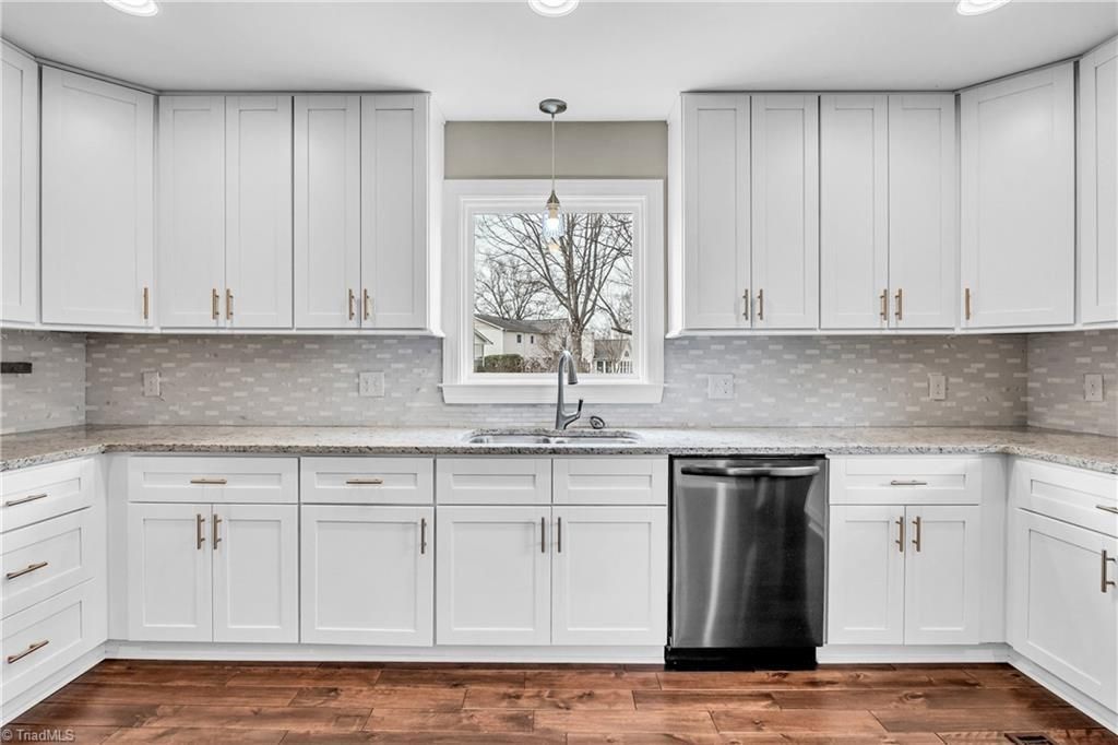 Modern white kitchen with gray cabinets, stainless dishwasher, and central window above sink