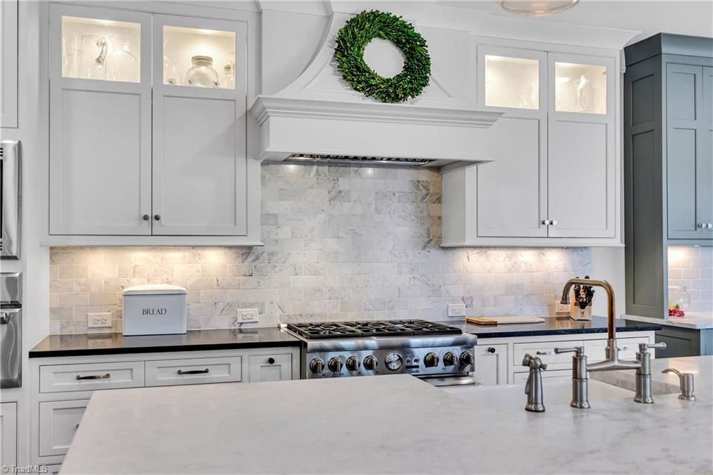 Bright white kitchen with marble island, stainless range, gray cabinets, and a green wreath above the stove