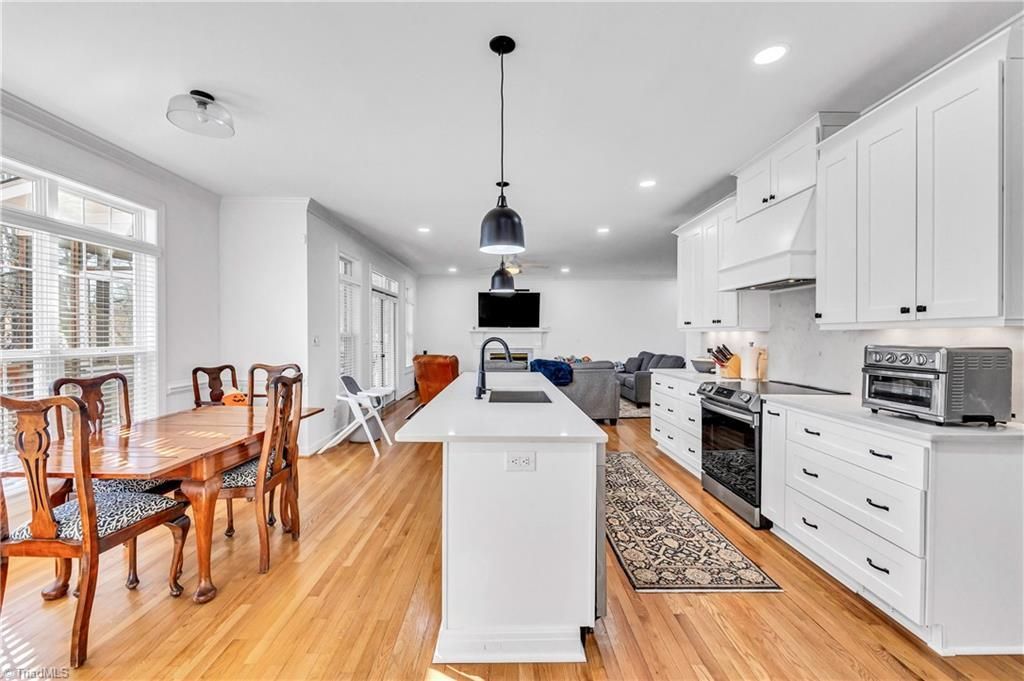 Bright white kitchen and dining area with wood floors, island, black pendant light, and wicker chairs