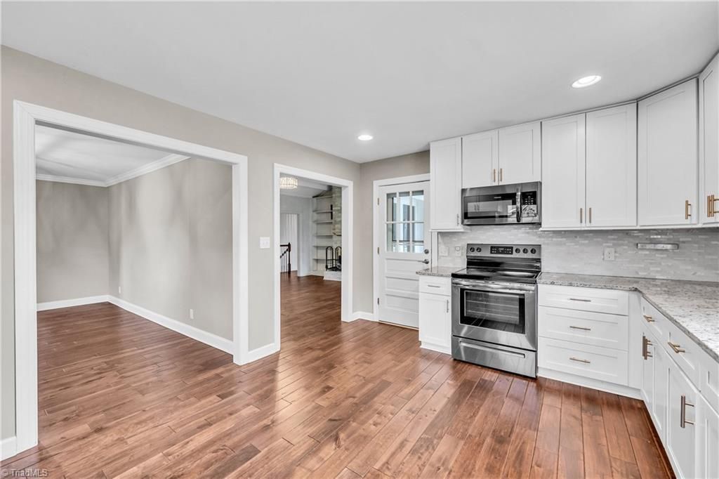 Bright modern kitchen with white cabinets, stainless steel appliances, and hardwood floors opening to a dining area