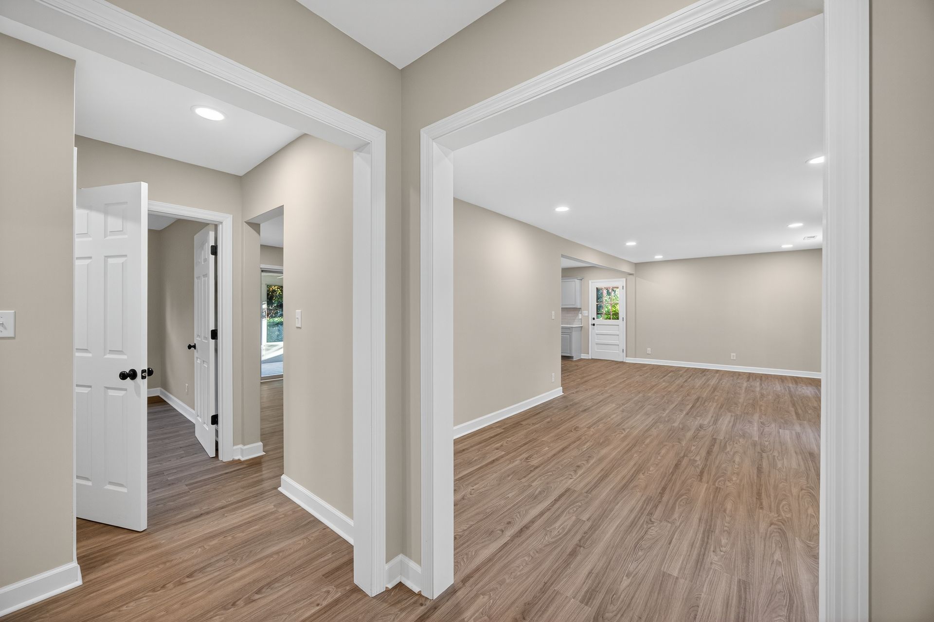 Empty modern interior with beige walls, wood-look floors, and open doorways to adjacent rooms
