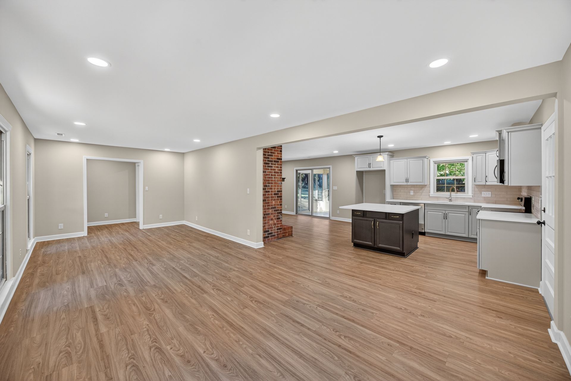 Empty open-plan living room and kitchen with wood floors, white walls, and recessed lighting
