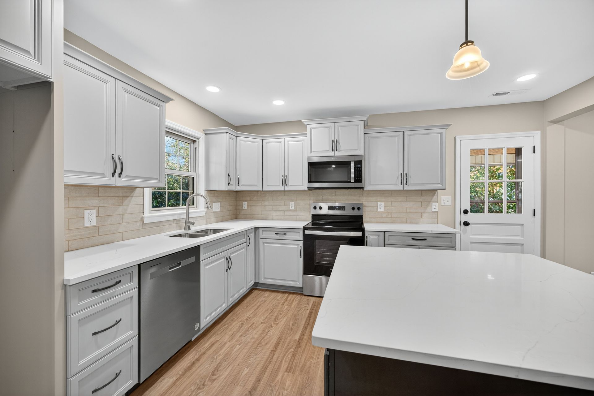 Bright modern kitchen with white cabinets, stainless appliances, wood floors, and a large island.