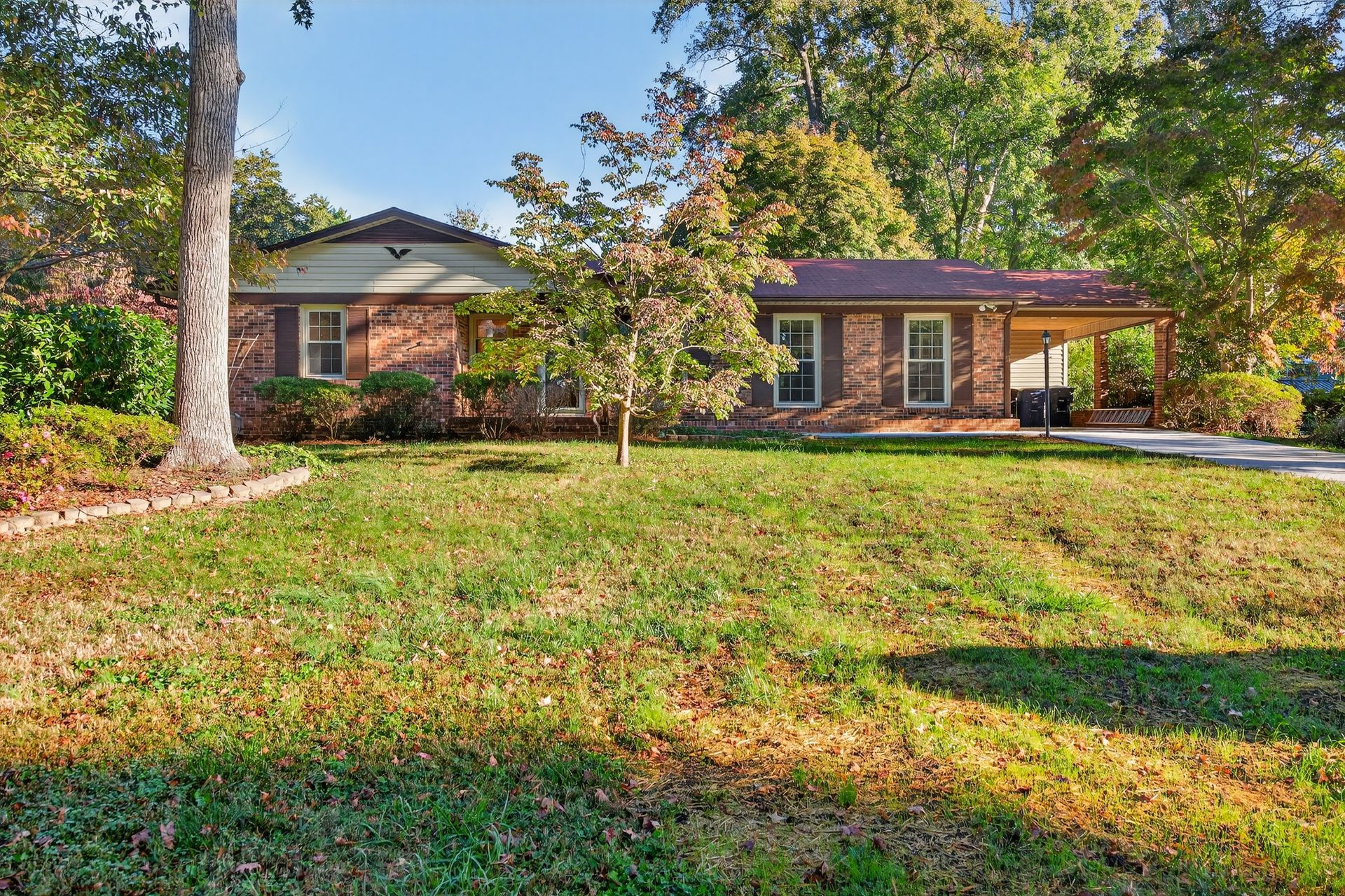 Single-story brick house with a large front lawn and trees on a sunny day