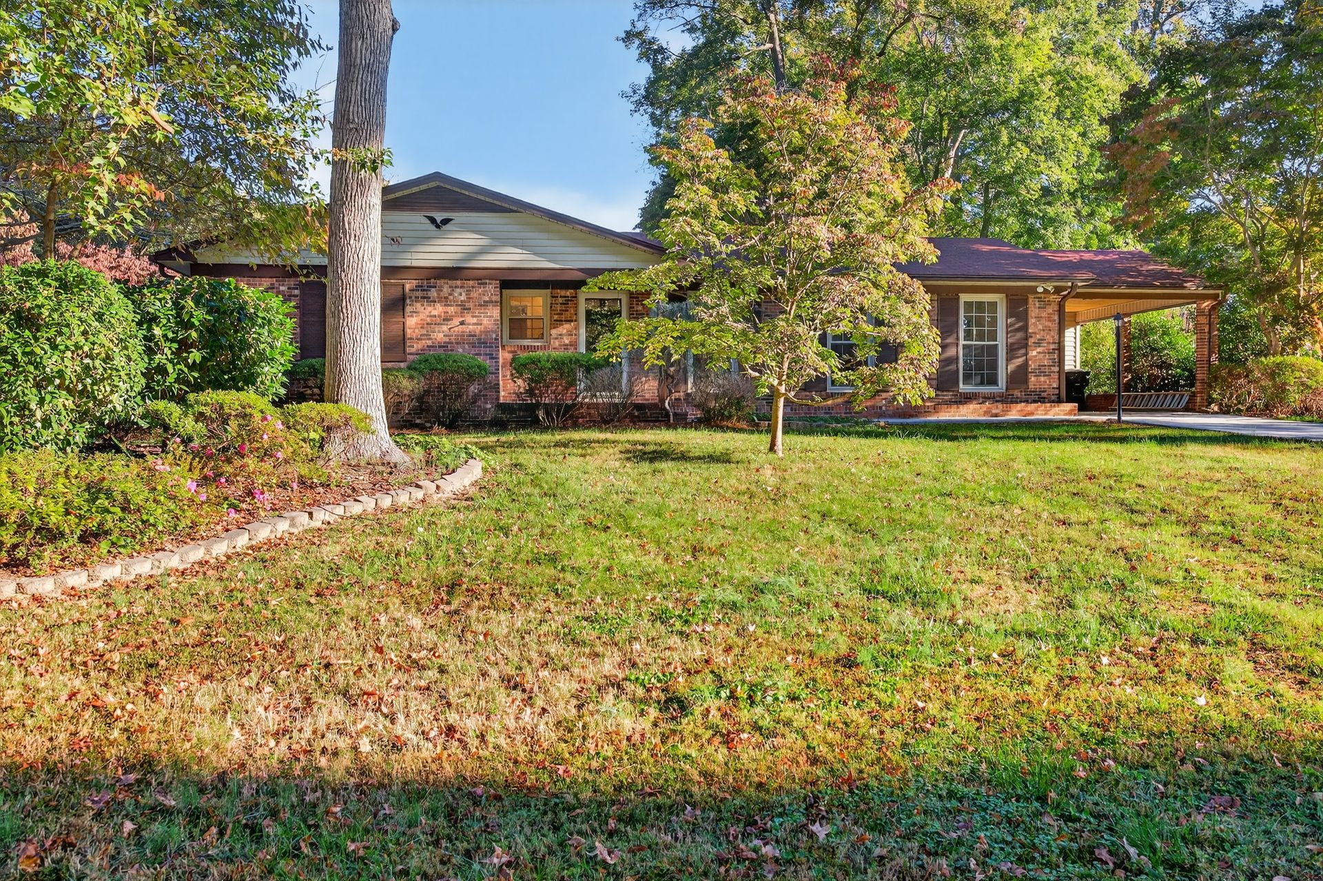 Single-story brick house with a large green lawn and trees in the front yard.