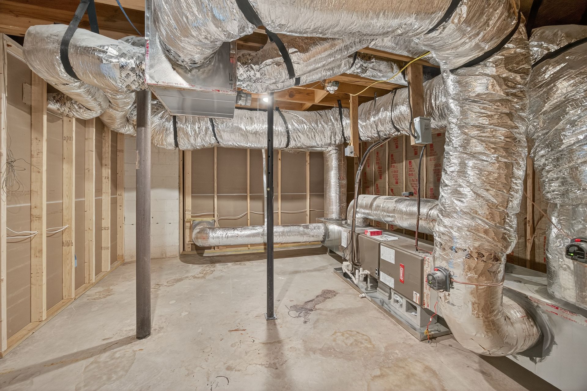 Unfinished basement with exposed ducts, insulation, and support posts around a suspended rectangular frame.