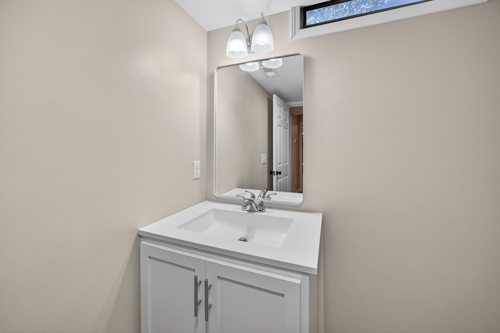 Small beige bathroom vanity with white sink, mirror, and overhead light fixtures