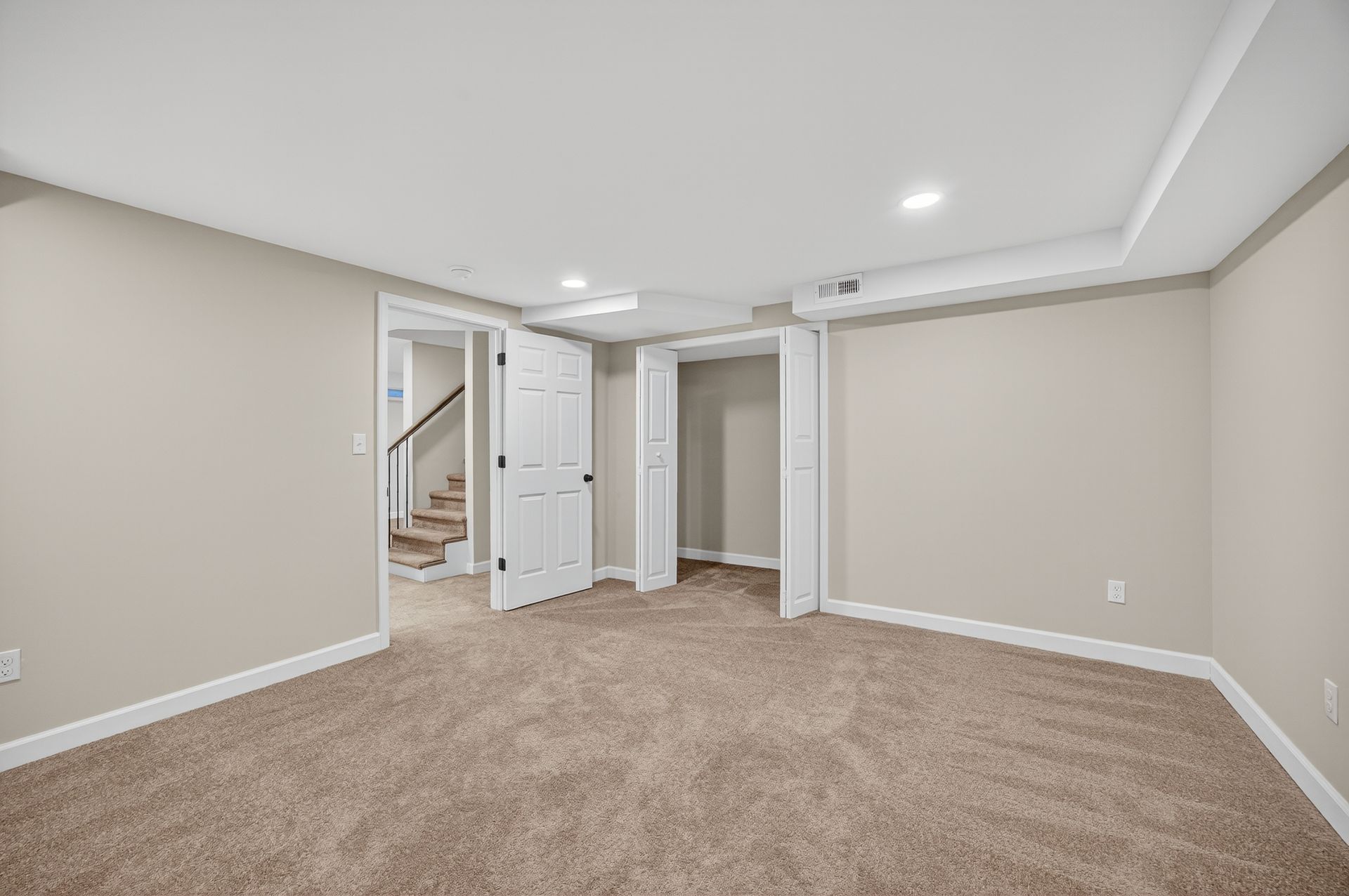 Empty beige carpeted room with white trim, open doors, and recessed ceiling lights