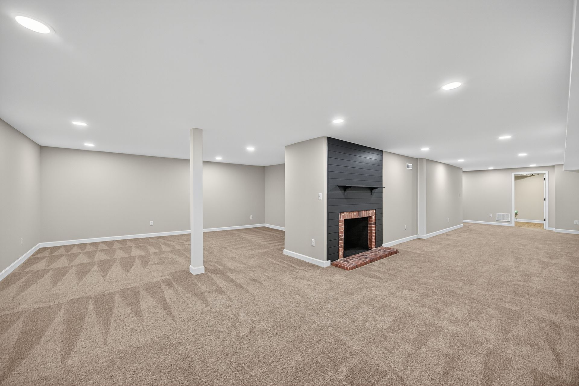 Spacious carpeted basement with recessed lights, white columns, and a dark fireplace centerpiece.