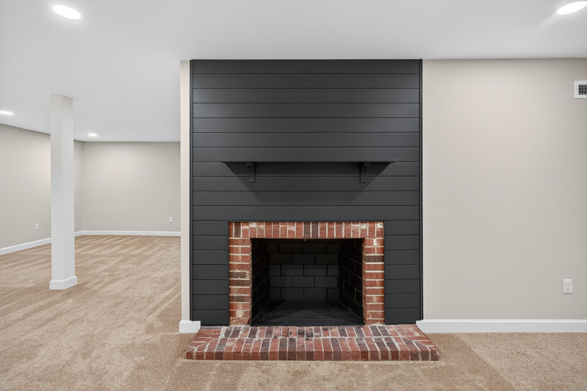 Empty living room with brick fireplace, dark shiplap accent wall, and beige carpet