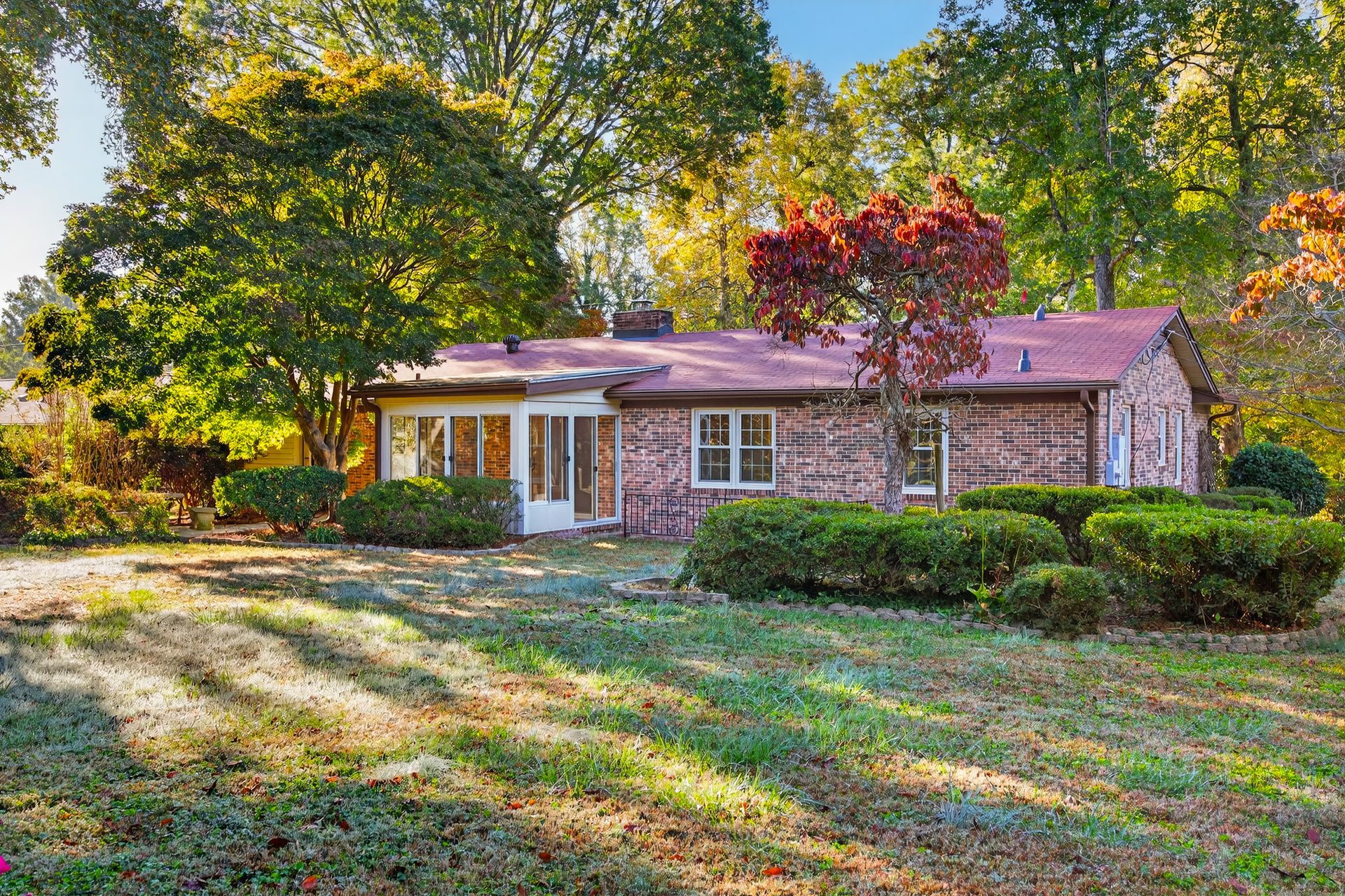 Small brick house with white porch set among trees and autumn foliage in a yard.