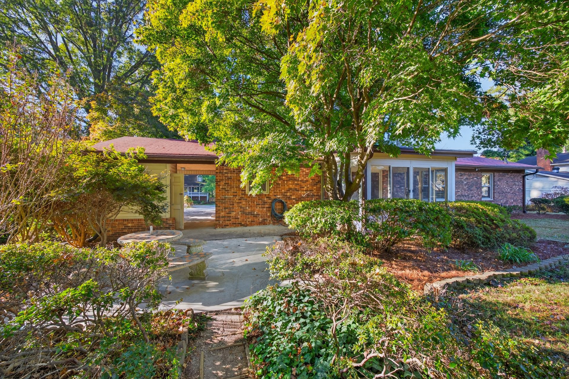 Suburban house with a brick facade, large tree, and landscaped front yard in bright sunlight