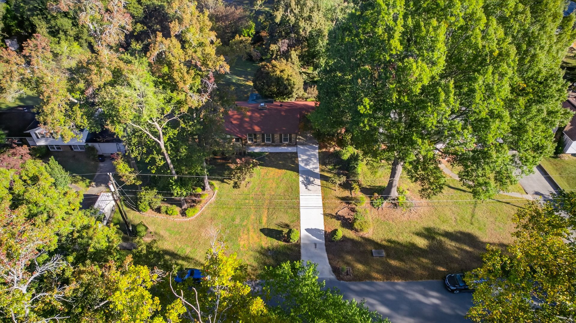 Aerial view of a wooded park with a path leading to a small building and road.