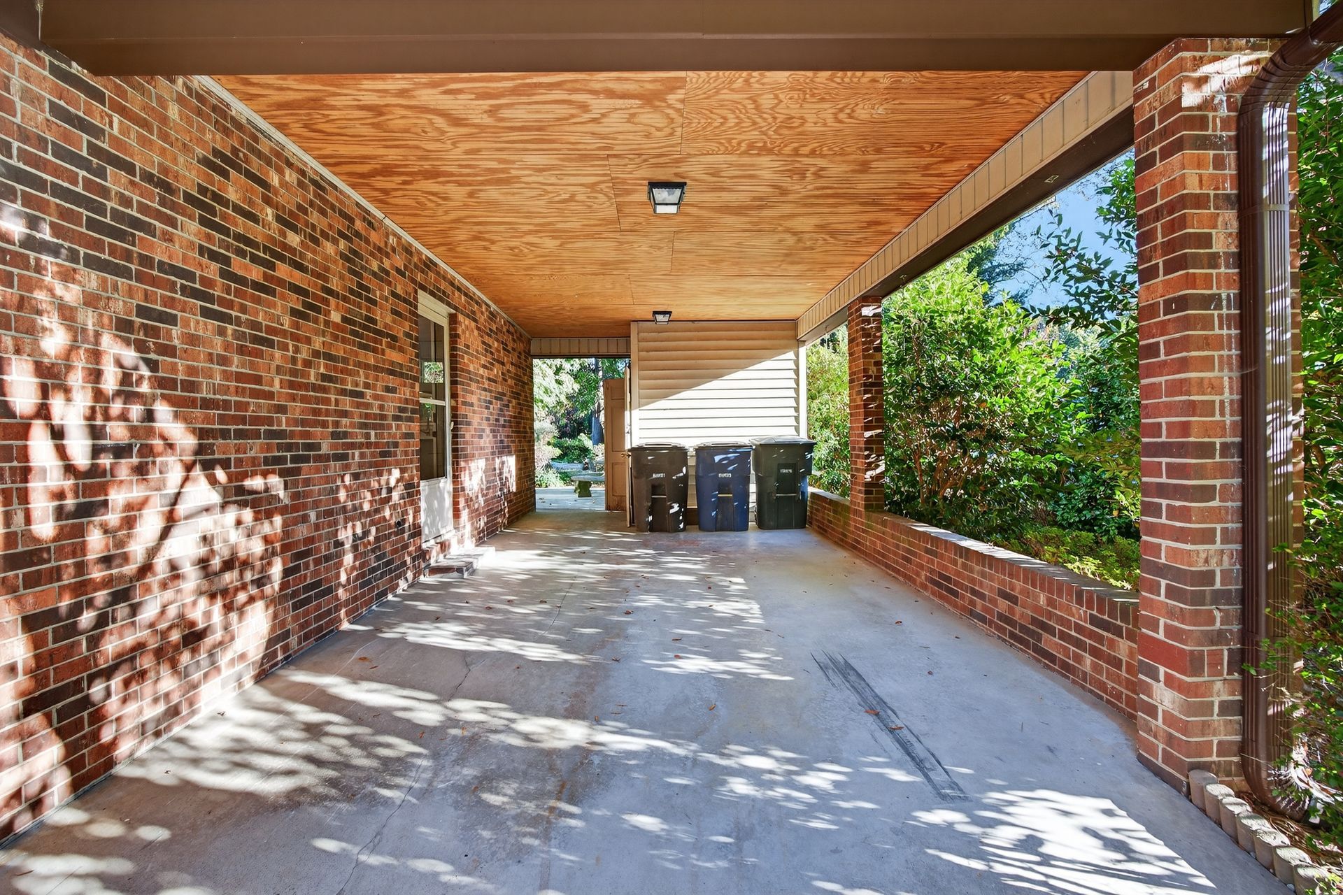 Covered brick patio with wood ceiling, concrete floor, and sliding doors at the end