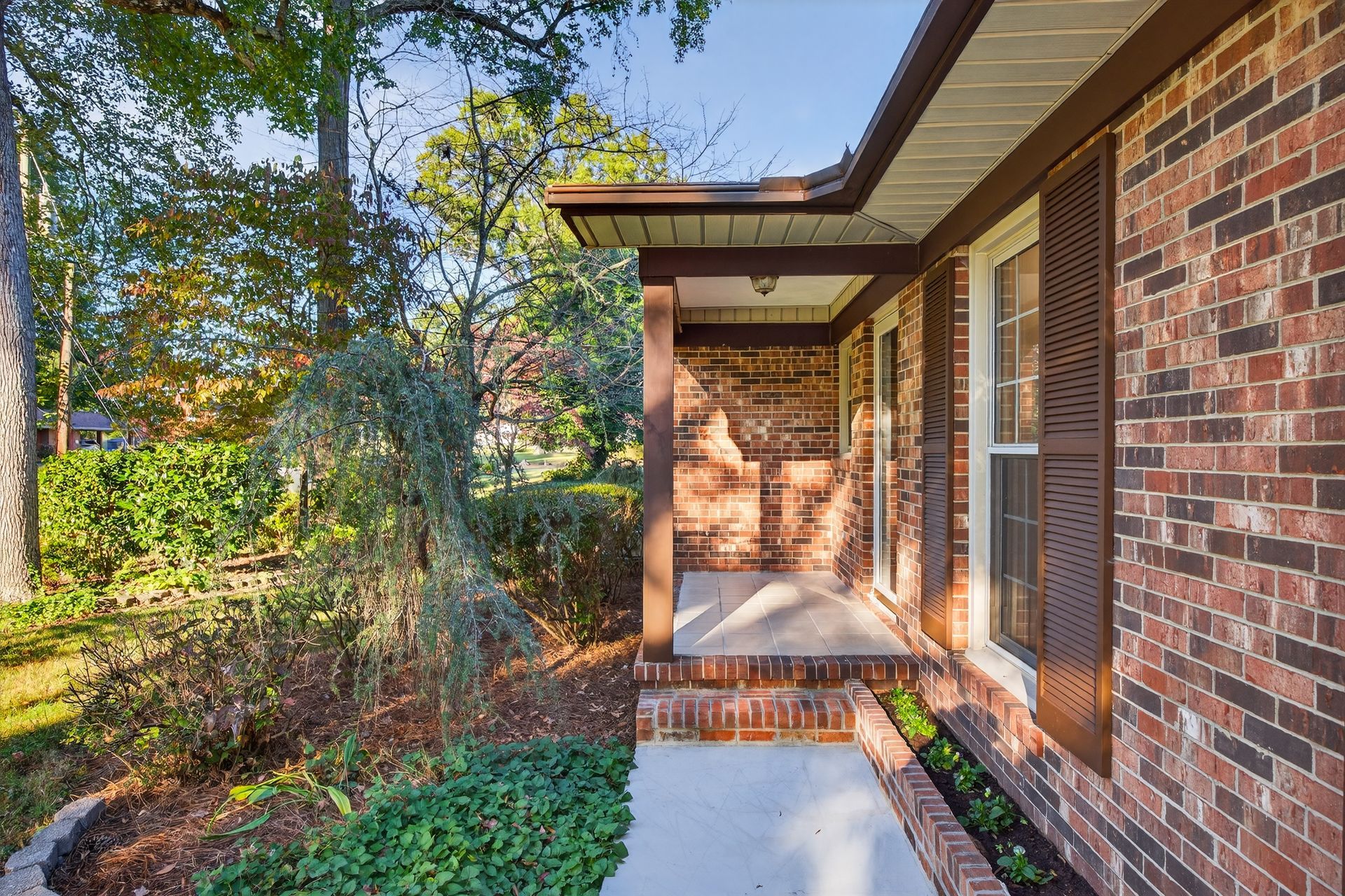 Brick house porch with a concrete walkway, brick pillars, and trees in the yard