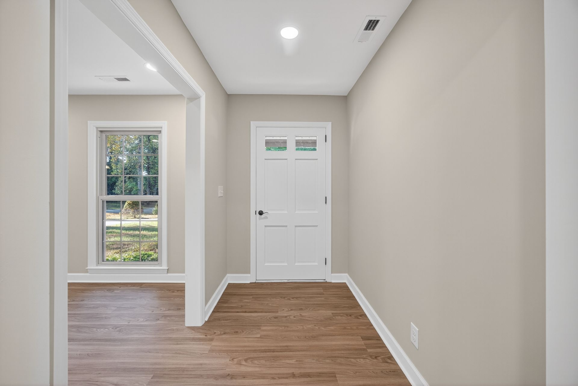Empty hallway with beige walls, wood floors, and a white front door at the end