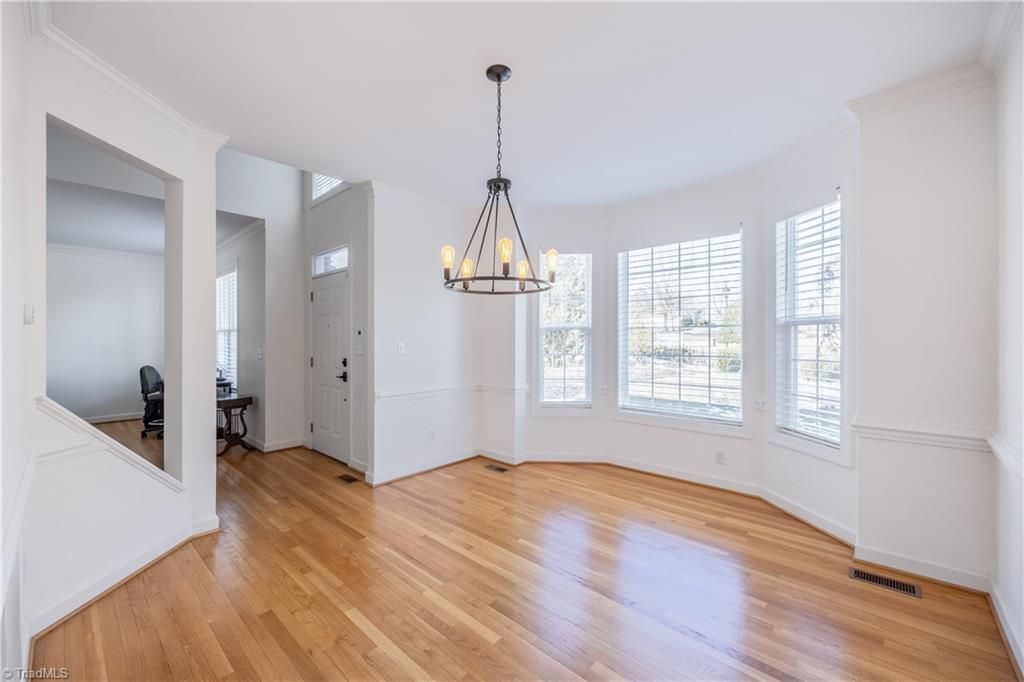 Bright empty dining room with hardwood floors, chandelier, and large windows with white trim