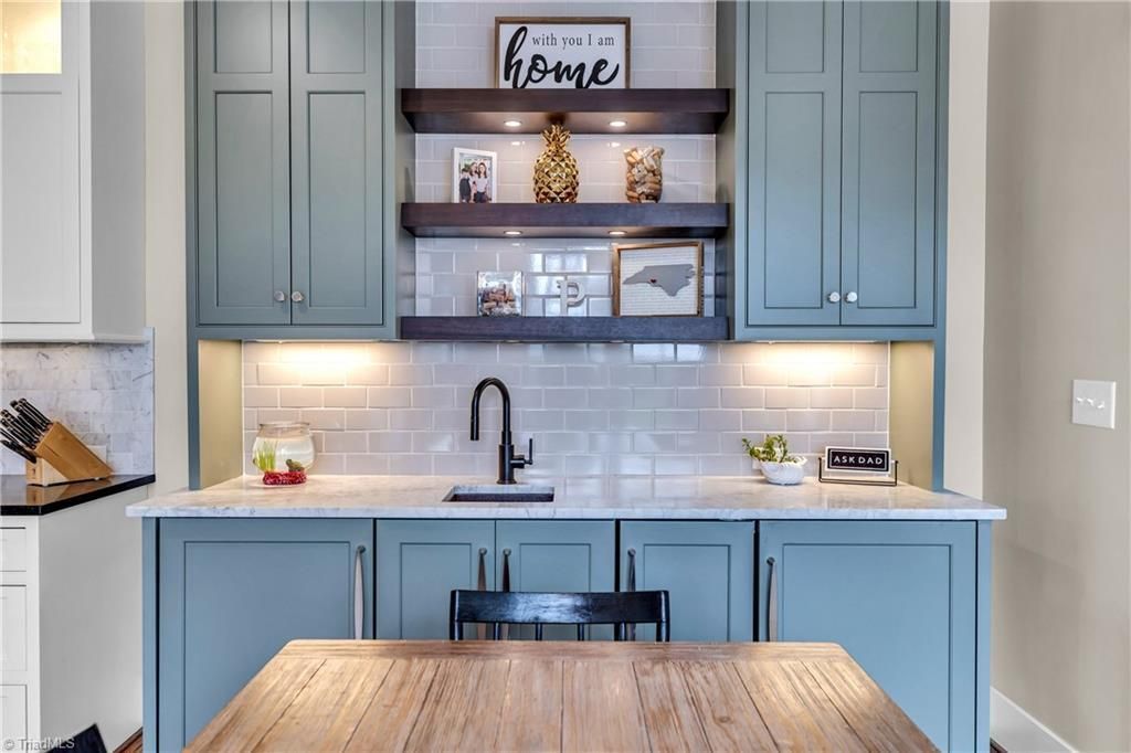 Blue kitchen with wood table, open shelves, and a sink under white subway tile backsplash