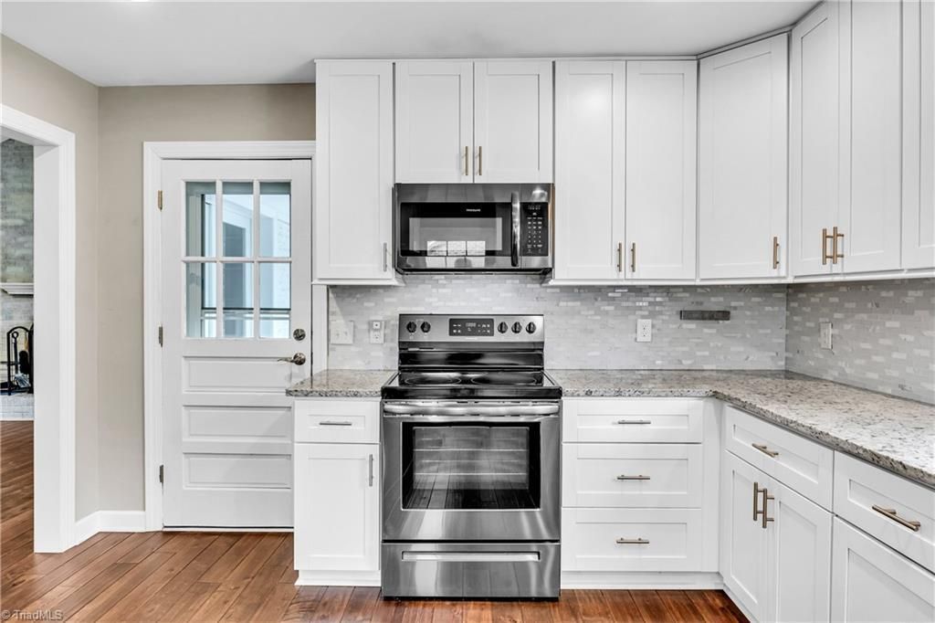 Bright white kitchen with stainless steel stove, microwave, and cabinets, plus wood floors and gray backsplash