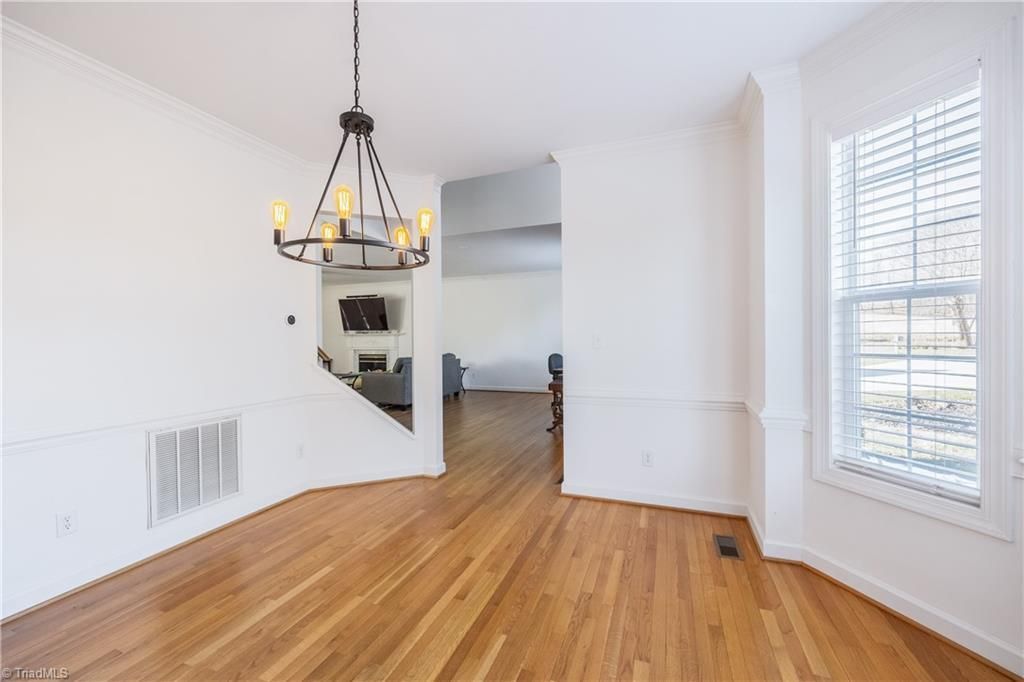 Bright empty dining room with hardwood floors, white walls, chandelier, and a window with blinds.