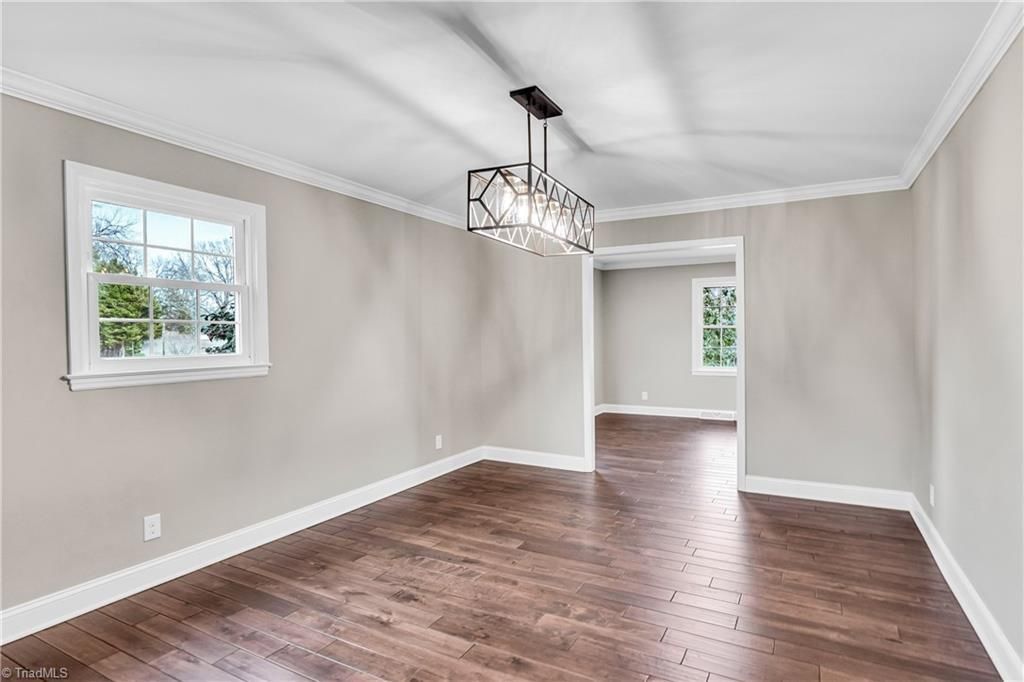 Empty beige dining room with hardwood floors, white trim, and chandelier lighting.