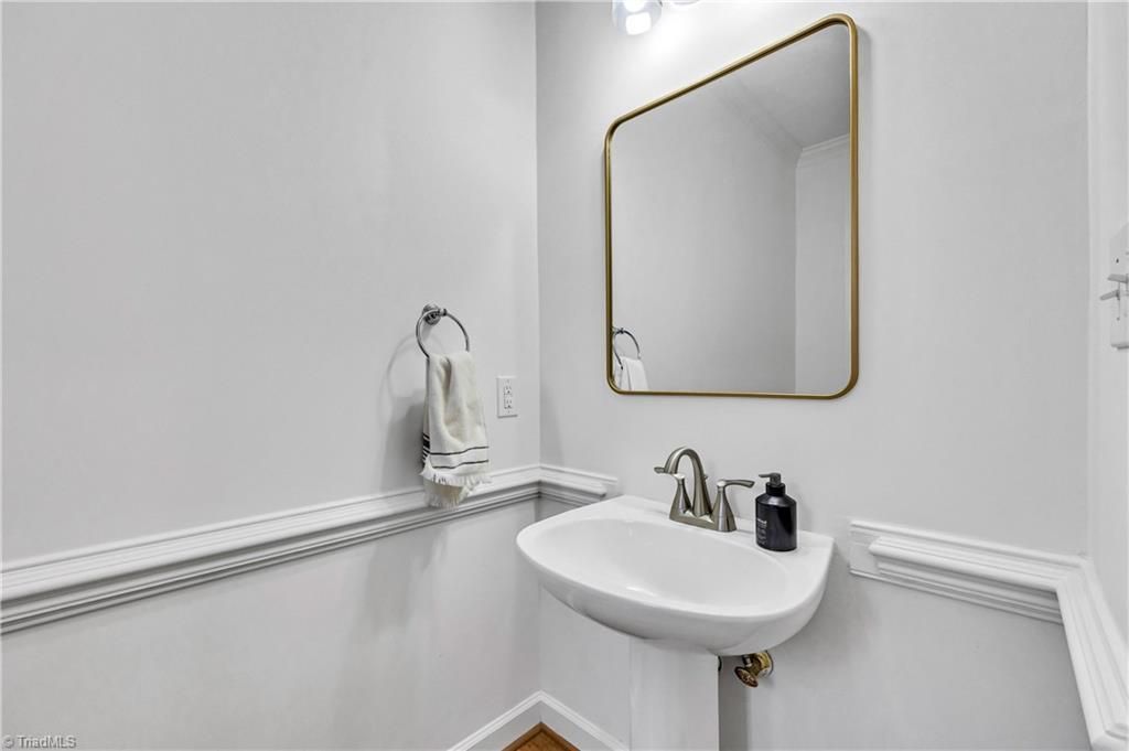 Small white bathroom with pedestal sink, gold-framed mirror, and decorative chair rail molding